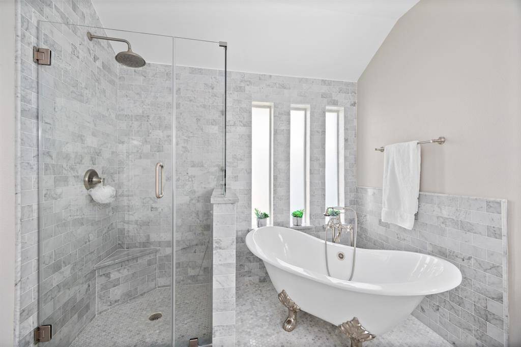 Custom clawfoot tub with vintage-inspired faucet, marble mosaic floors, marble subway tile, seamless glass shower, and marble-topped vanities.