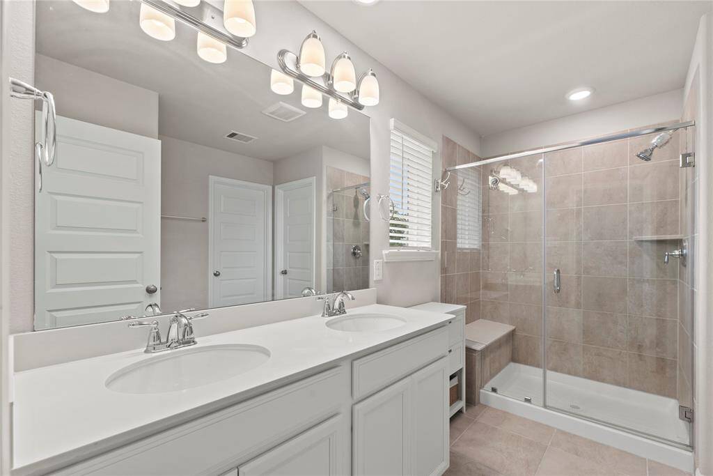 The primary bath features dual vanities, providing ample personal space along with an abundance of custom cabinetry for seamless organization. The expansive walk-in shower, adorned with stunning tile work and a sleek glass front, offers a luxurious escape for a quick rinse or a refreshing retreat.