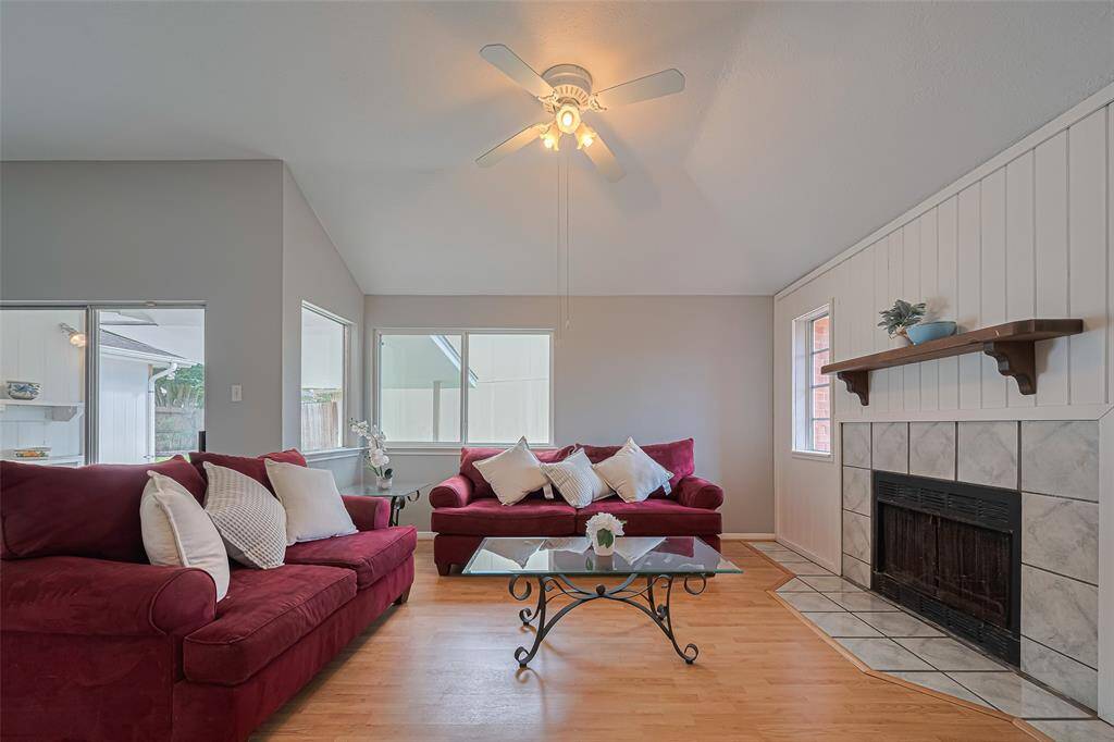 Anchored by a white paneled accent wall with a fireplace, this luminous living room is framed by oversized windows and finished with sleek wood-style flooring and a ceiling fan.
