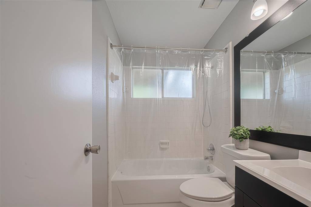 The wide mirror above the vanity is framed in a sleek black, while a combination shower and tub offers comfort and utility in one elegant space.