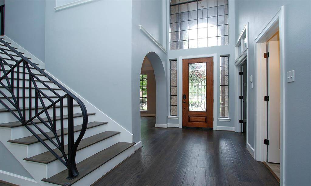 The first floor features rich dark brown wood flooring; a wide staircase with elegant iron balusters leading to the second floor.
