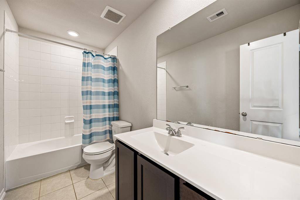 Secondary bathroom features light countertops and cabinets, custom paint, shower/tub combo with tile surround, large mirror, tile floors, sleek fixtures and modern finishes, plenty of space to accommodate any visiting family or guests.