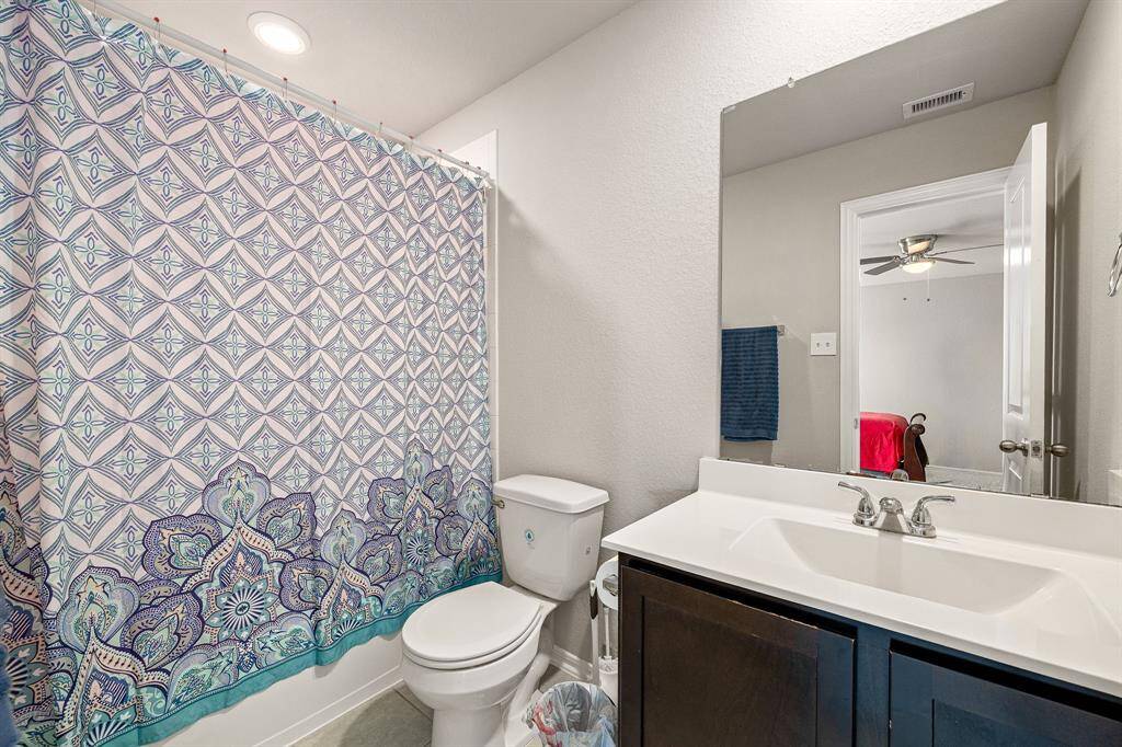 Secondary bath features tile flooring, bath/shower combo with tile surround, dark wood cabinets, beautiful light countertops, mirror, dark, sleek fixtures and modern finishes.