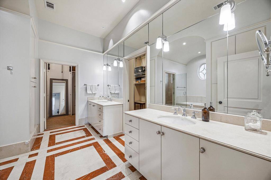 Dual vanities with full-wall mirrors, granite counters, and ample storage lead into a spacious walk-in closet for effortless organization.