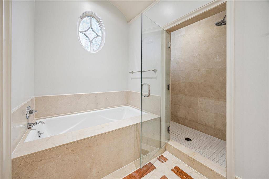 Enjoy spa-like relaxation with a soaking tub beneath a decorative window and a frameless walk-in shower.