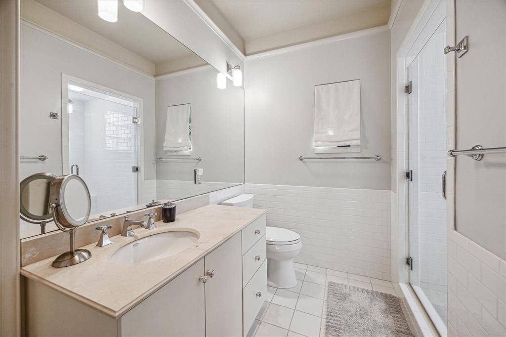 Crisp and classic, the secondary bath includes a spacious walk-in shower, neutral tile finishes, and a wide vanity with ample storage.