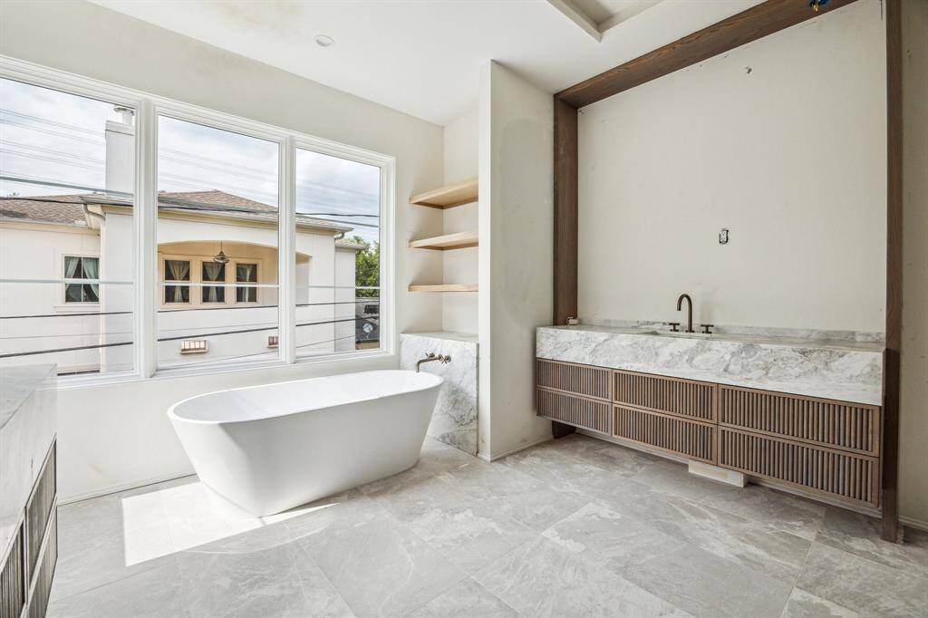 A closer view of the free-standing tub with a wall mounted tub filler and open shelving for additional storage.