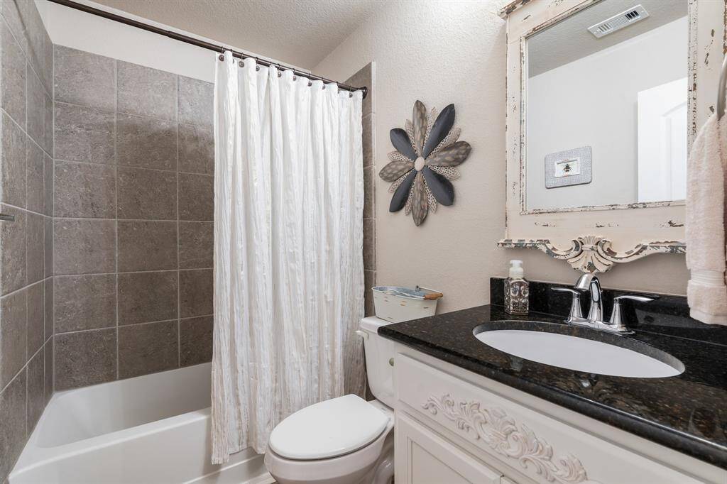 This bathroom features a classic design with a tiled shower and bathtub, elegant granite countertop, and a vintage-style mirror.