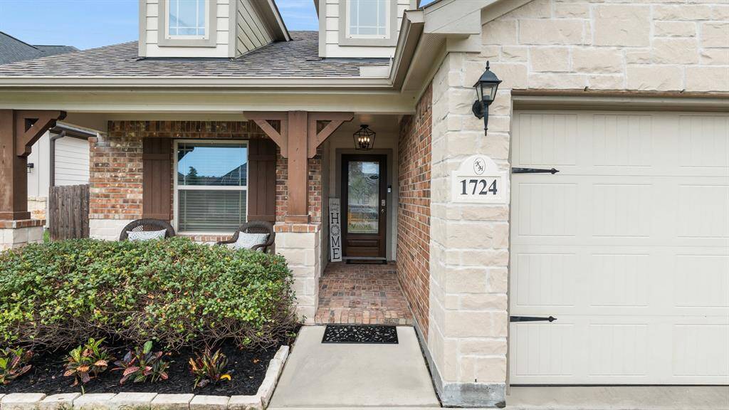 welcoming front porch featuring brick and stone facade, and modern garage with carriage-style lighting.