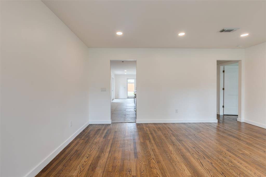 This photo showcases a bright, open room with polished hardwood floors and recessed lighting. The space leads to a tiled area with a view of a window, offering a modern and clean aesthetic.