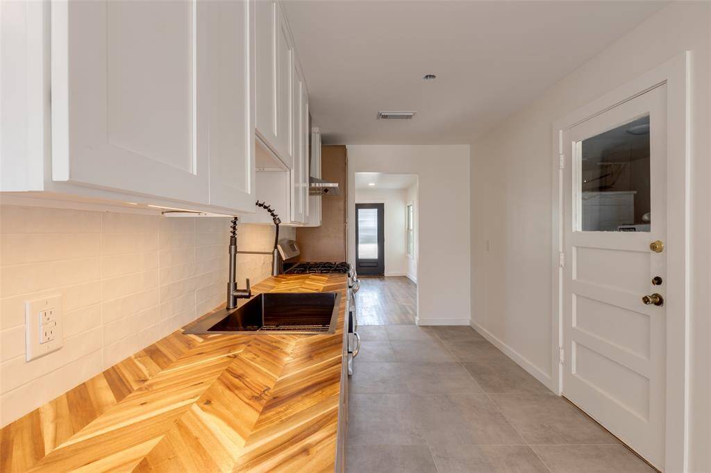 This new kitchen features a sleek design with white cabinetry, a stylish herringbone wood countertop, and modern fixtures. It has ample natural light and access from the living room into the adjoining dining room.