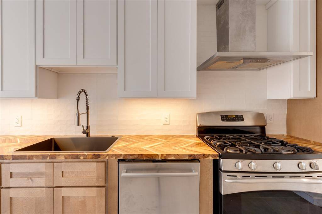 New kitchen with a stylish herringbone wood countertop, stainless steel appliances, and sleek white cabinets. It features a deep sink with a contemporary faucet and under-cabinet lighting for a bright, inviting space.