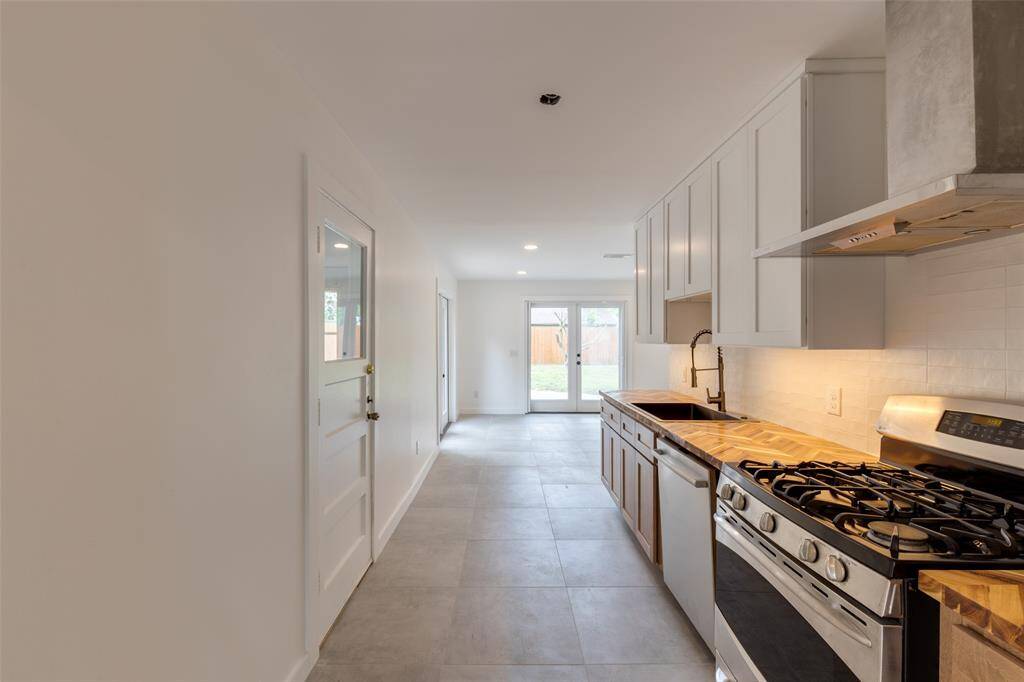 This photo shows the renovated kitchen with a sleek gas range, light cabinetry, and ample counter space. It has a bright, open layout leading to a dining area with large windows and a door opening to the backyard, providing plenty of natural light.