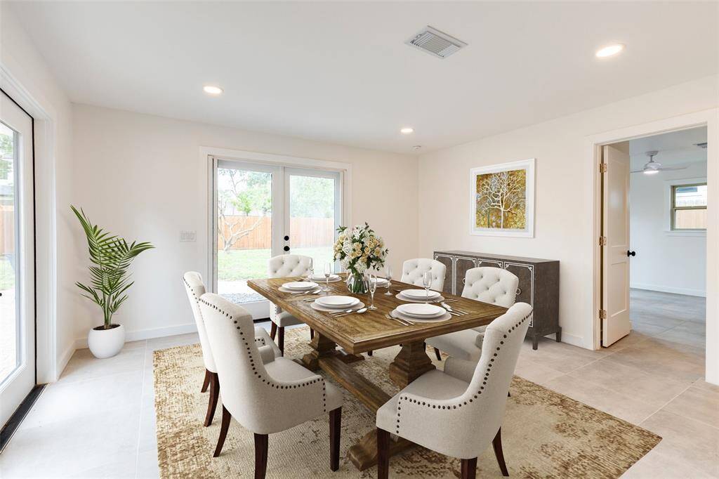 This virtually staged bright dining room features a rustic wooden table with elegant, upholstered chairs, set on a subtle area rug to show the design potential. Natural light pours in through large glass doors leading to a backyard, enhancing the room's airy feel. A virtually staged decorative sideboard and wall art add charm, while a potted plant brings a touch of greenery to show the design potential of the room.