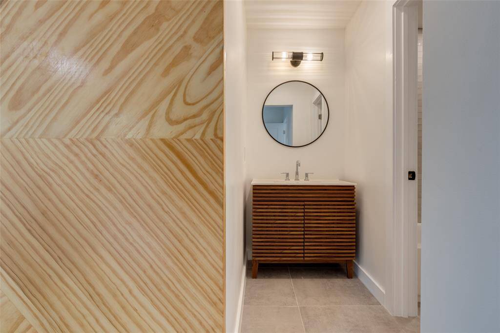 This photo shows the new modern en-suite bathroom featuring a stylish wooden vanity with horizontal slats, a round mirror, and sleek lighting. The space has a light, neutral color palette and a contemporary design.