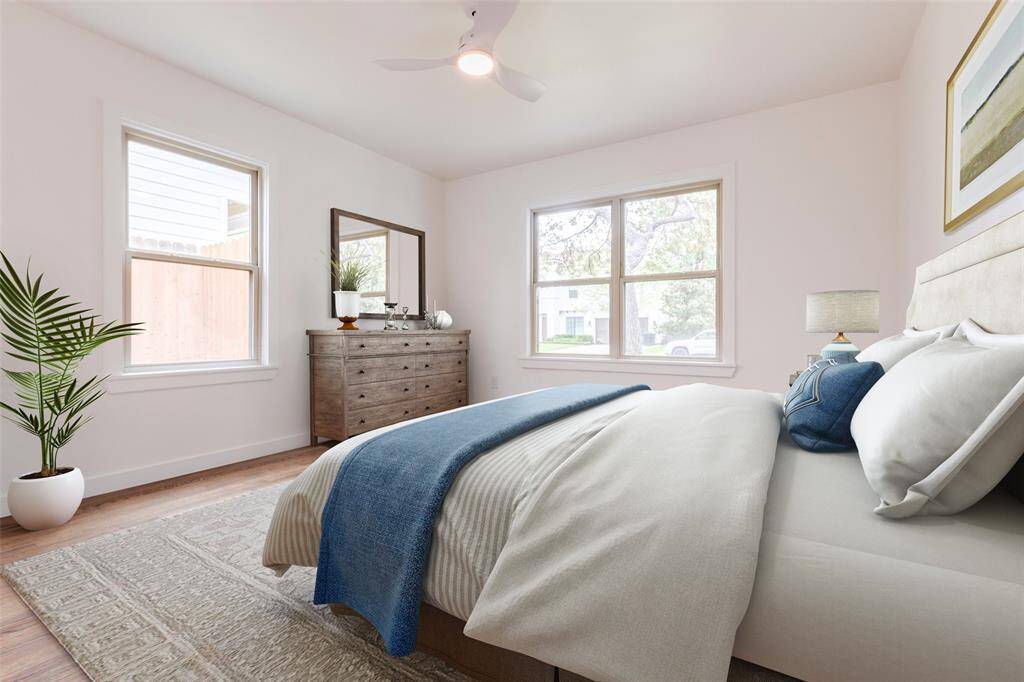Bright and airy virtually staged secondary bedroom with large windows, hardwood floors, and neutral walls. The virtually staged bedroom features a cozy bed with blue and white bedding, a stylish dresser with a mirror, and a potted plant for a touch of greenery to show the design potential of the bedroom.