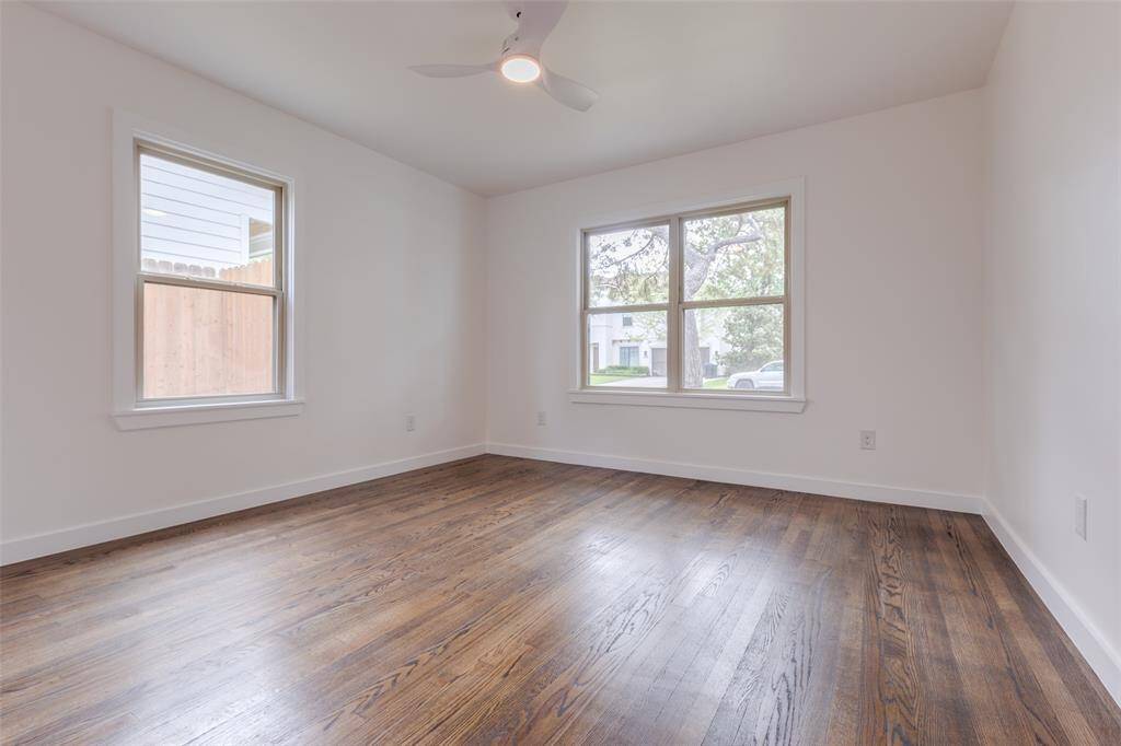 Bright, spacious room with hardwood floors, large windows offering natural light, and a ceiling fan for comfort. Perfect for a bedroom or office.