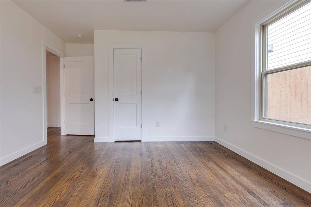 This photo shows another view of the bright secondary bedroom with hardwood floors, white walls, and a large window. It's a clean, versatile bedroom space ready for personalization.