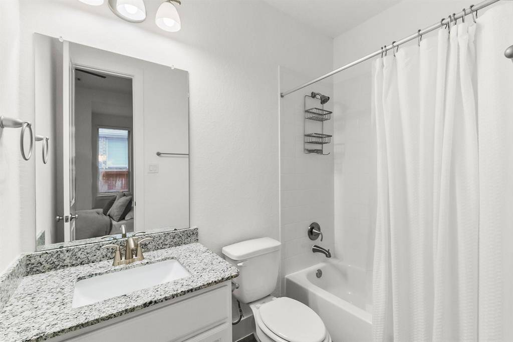 En-suite bathroom for this bedroom features wood-look tile plank flooring, rectangular undermount sink with granite countertop, toilet, tiled shower/tub combo, and hallway linen closet.