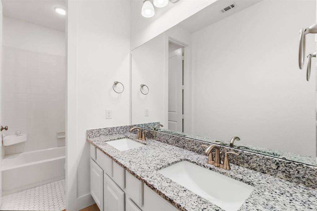 The third full bathroom for Bedrooms 3 and 4 features dual undermount sinks with granite counter top, wood  flooring, and a private tiled area with toilet and tiled shower/tub combo. There is also a large closet in the hallway for linen storage.