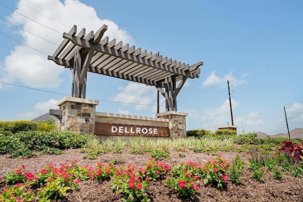 The entrance to the Dellrose community, featuring large stone monuments with "Dellrose" inscribed on them, surrounded by well-maintained landscaping including palm trees. It gives a grand and welcoming first impression to this master-planned community in Hockley, TX.Sources