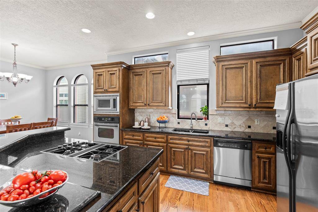 Open concept kitchen with a central island and gas cooktop. Black granite countertops, stainless steel appliances and storage galore. Central island provides more workspace, storage, and a social hub within the kitchen.