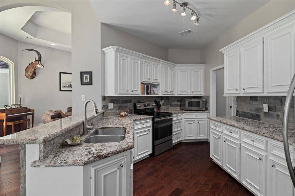 This photo showcases a modern kitchen with upgraded white cabinetry, granite countertops, stone backsplash, cabinet hardware, stainless steel appliances, dual sink with stainless fixtures, and ample storage.  Refrigerator and counter microwave stays!