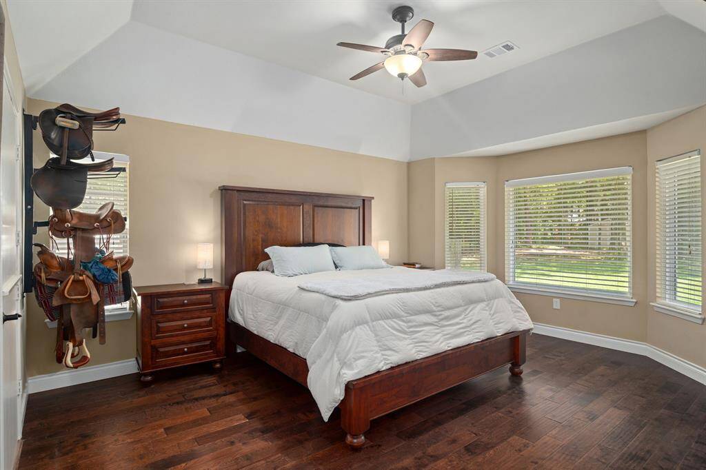 A spacious bedroom featuring hardwood floors and large windows with views of the backyard, offering ample natural light. It also includes a ceiling fan