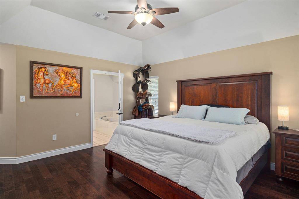 This bedroom features a vaulted ceiling, a ceiling fan, and hardwood floors. An open doorway leads to your ensuite bath