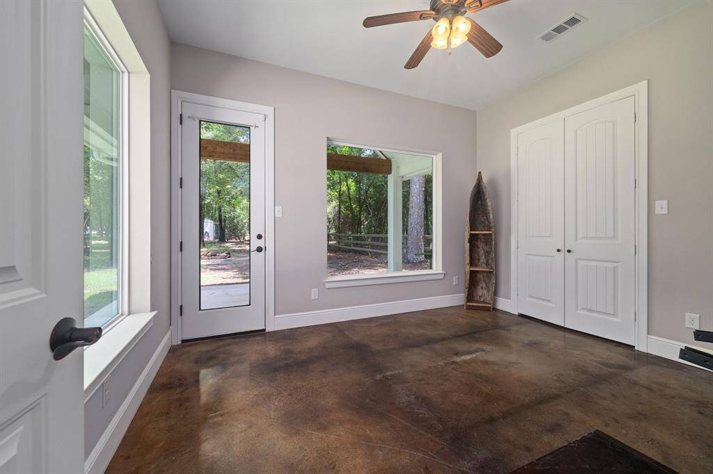 Guest Room main bedroom with large picture windows and a glass door leading outside to a huge covered patio. It features high ceilings, ceiling fan, large dbl door closet, and polished concrete floors, creating a modern and airy feel