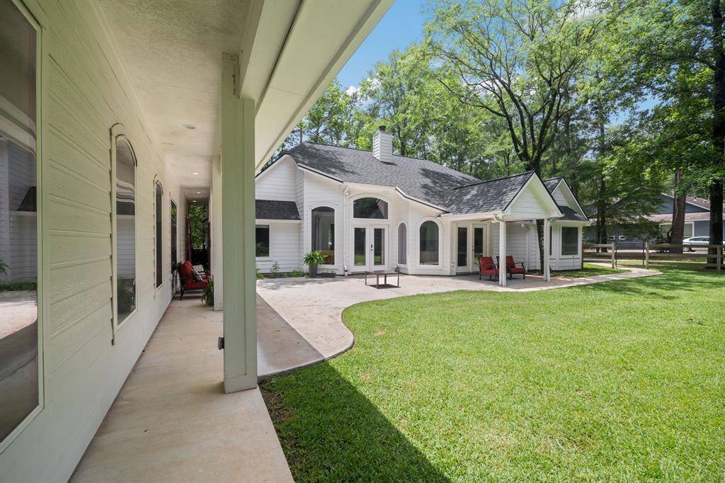 This photo showcases a charming, spacious backyard with a well-maintained lawn and a covered patio. The house features large windows, a modern design, and is surrounded by lush trees, offering a peaceful outdoor living space.