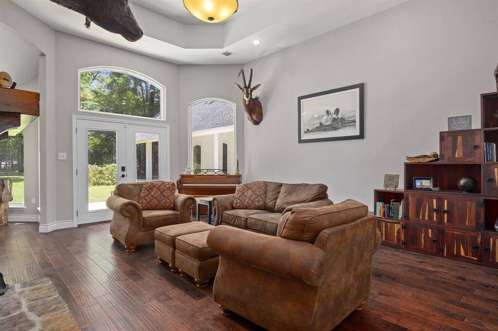 This cozy living room features upgraded engineered hardwood floors and high ceilings with tray accents The space is brightened by the large windows and a glass doors leading to the outdoor area.