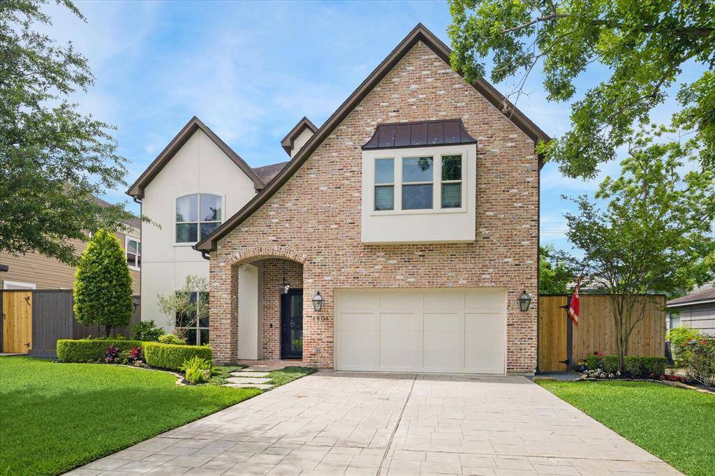 Charming entryway framed by a classic brick arch and accented with warm lantern-style lighting. A wrought iron and glass front door adds a touch of elegance, while the thoughtfully landscaped path invites you in with lush greenery, manicured hedges, and vibrant seasonal flowers.