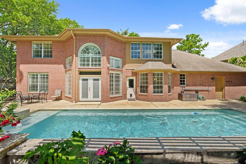 This photo showcases a spacious brick home with a large backyard POOL/SPA, surrounded by a patio area perfect for outdoor dining and relaxation. The home features expansive windows and offers a blend of comfort and style.