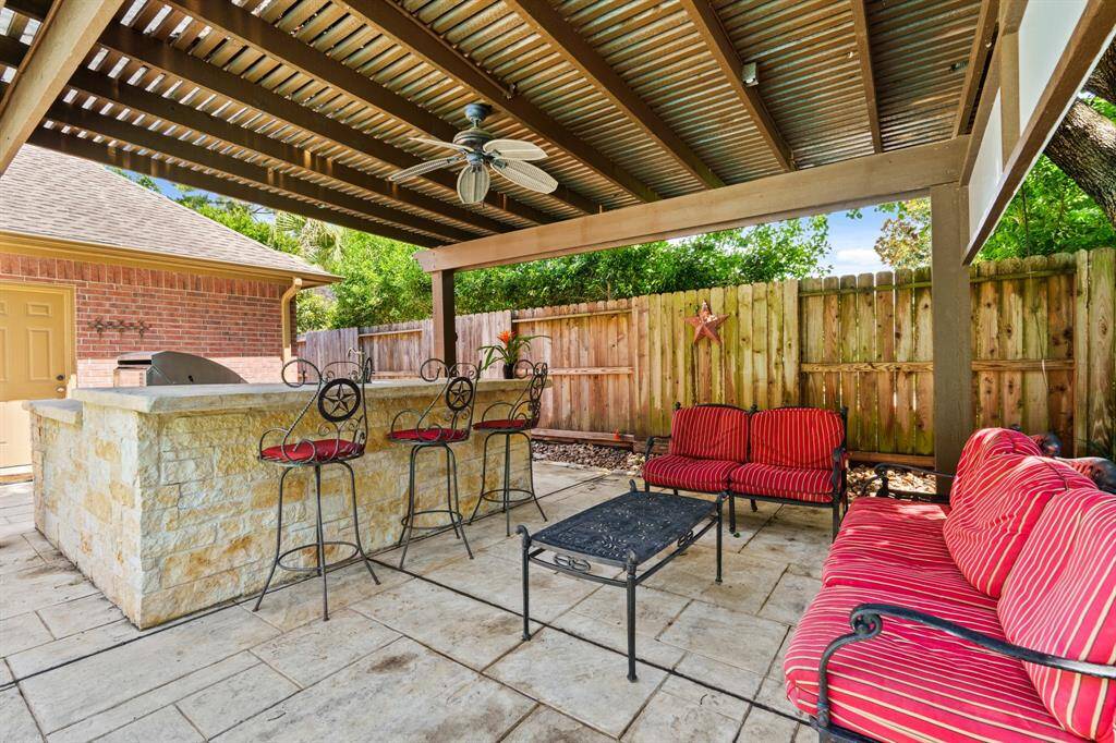 This outdoor space features a covered patio with a built-in grill, sink, mini fridge, ceiling fan, bar seating, and a stone countertop.  Enjoy evenings, weekends and holidays overlooking the sparkling oasis.