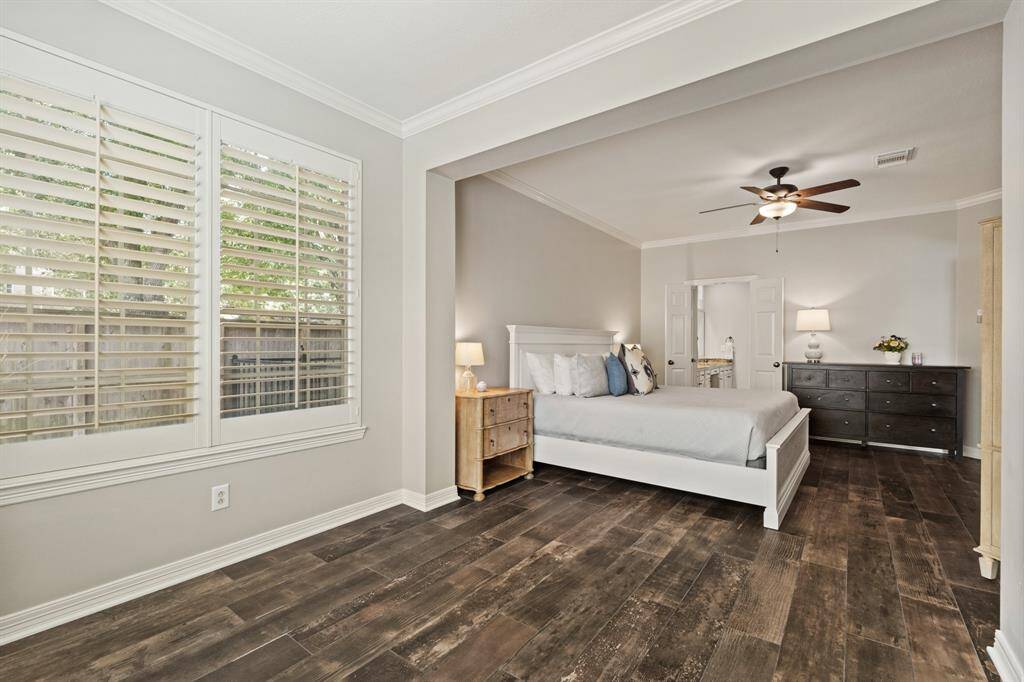 Spacious bedroom with tile wood like flooring and neutral-color walls. Features a large window with shutters overlooking the POOL/SPA, providing ample natural light and an adjacent door leads to the ensuite bathroom.