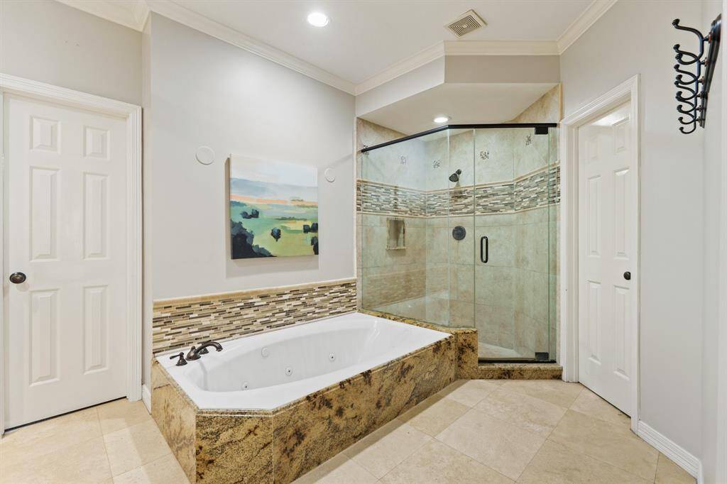 Another view of this bathroom features a luxurious spa tub with intricate tile accents and a spacious glass-enclosed shower. The neutral color palette and recessed lighting create a serene, modern ambiance.