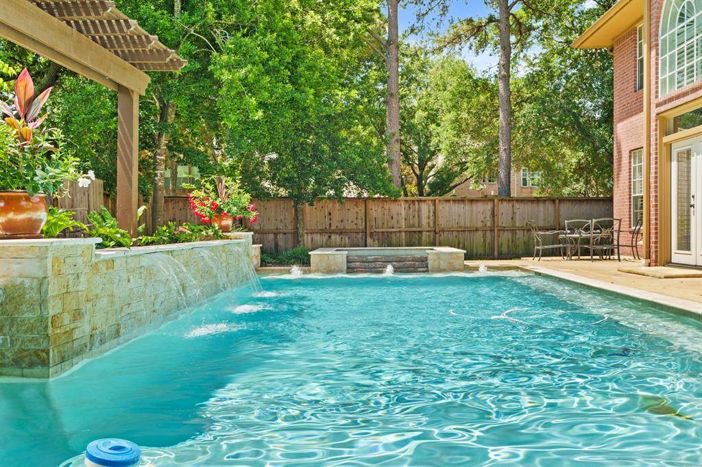 This backyard features a beautiful Swimming POOL/SPA with a cascading water feature, surrounded by lush greenery and a wooden pergola. A private, fenced area offers a serene and inviting space for relaxation and outdoor gatherings.