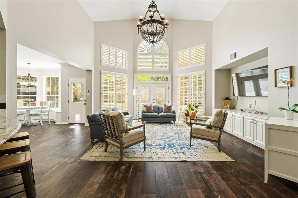 This spacious living room features high ceilings, large windows with shutters, and a central chandelier. It offers an open layout with tile wood like floors and is open to the Kitchen and breakfast bar seating area. Spectacular view of the POOL/SPA from the breakfast and living rooms.