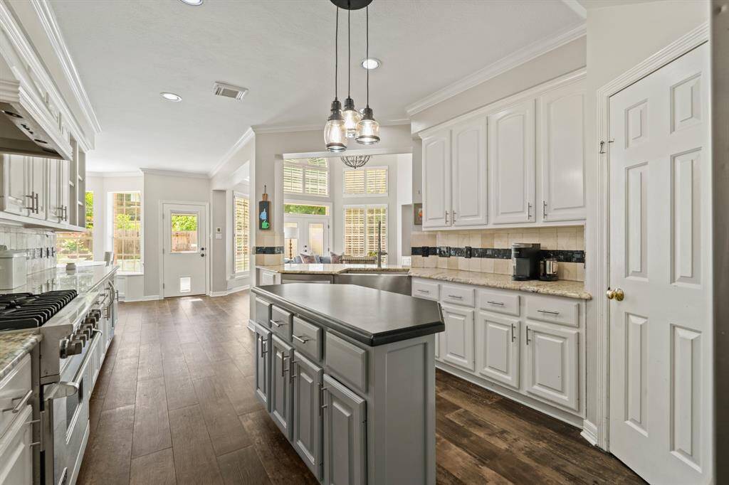 Another view of the spacious kitchen features modern white cabinetry, stainless steel appliances, and a large island with a solid surface countertop, tile wood like flooring, ample natural light from large windows.