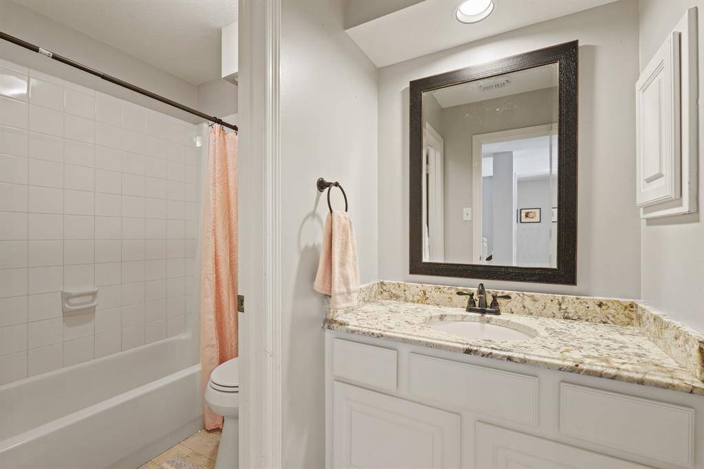 This full bathroom features a clean, modern design with a granite countertop, undermount sink, and a large mirror. It includes a tub-shower combo with a tiled surround and neutral color palette. Access from game room.