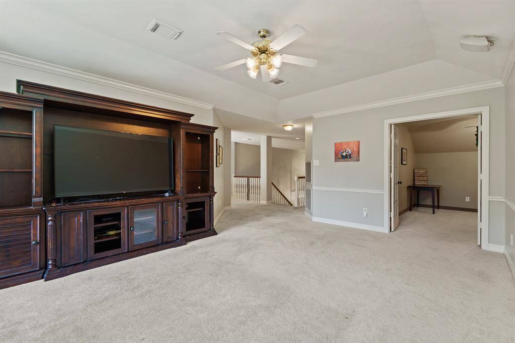 Another view of this spacious room features a large entertainment center with ample storage, and neutral carpeting. It opens to a hobby room, playroom or flex space. Overlooks a staircase, providing a versatile living area.
