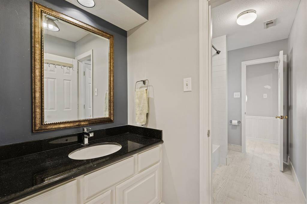 This Jack and Jill bathroom features a granite countertop with a modern sink, accented by a large, elegant mirror.  The room extends to a tiled tub/shower area, offering a clean look.