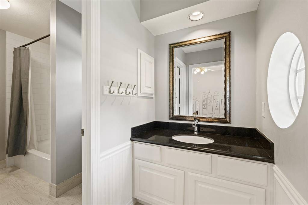 This bathroom features a sleek private vanity area with a black granite countertop, white cabinetry, and a framed mirror. It has a full tub/shower and modern fixtures, complemented by neutral-toned walls.