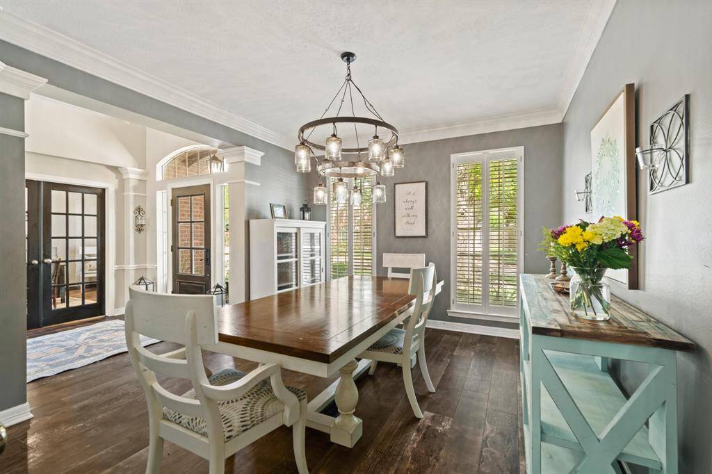 This dining room features elegant tile wood like floors and paint complemented by a modern chandelier. Natural light streams through large windows with shutters, and the decorative crown molding charm. Double doors lead to the study, enhancing the space's openness.