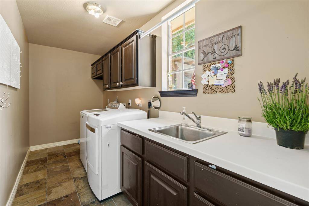 This laundry room features a washer and dryer hookup, ample countertop space, a sink, with plenty of cabinetry. The room is well-lit with natural light from a window, functional work space accessible from the kitchen and breakfast areas.