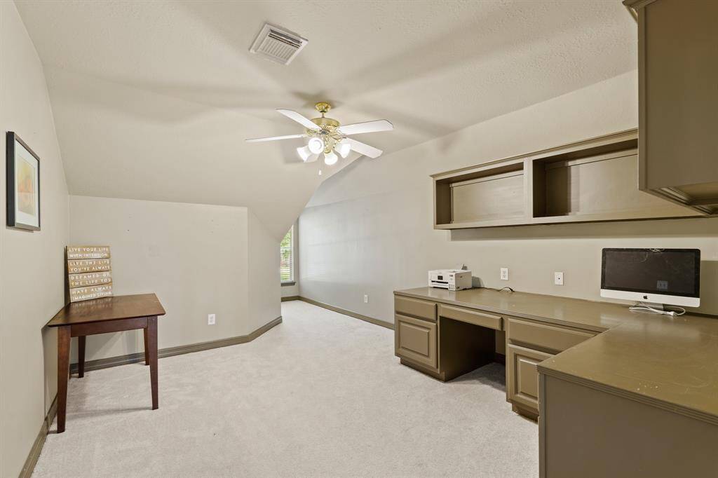 A spacious additional bedroom/flex room (crafting, additional home office or play/study space) with built-in cabinetry and desk, neutral walls, and carpet.  Open to the game room and full bath on the second level.
