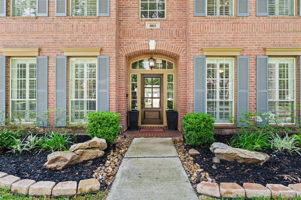 This photo showcases the wooden and glass front door entrance of the walkway lined with landscaping, and stone accents, nice curb appeal.