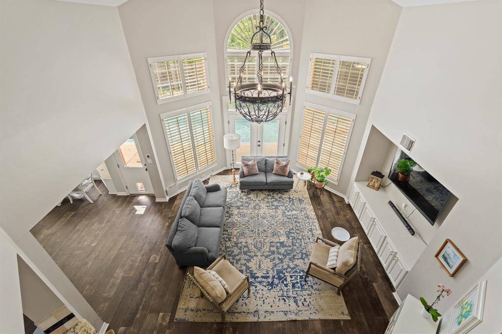 Living room features high ceilings and abundant natural light from large windows. It includes elegant tile wood like flooring, a stylish chandelier, and a built-in entertainment unit with cabinets.