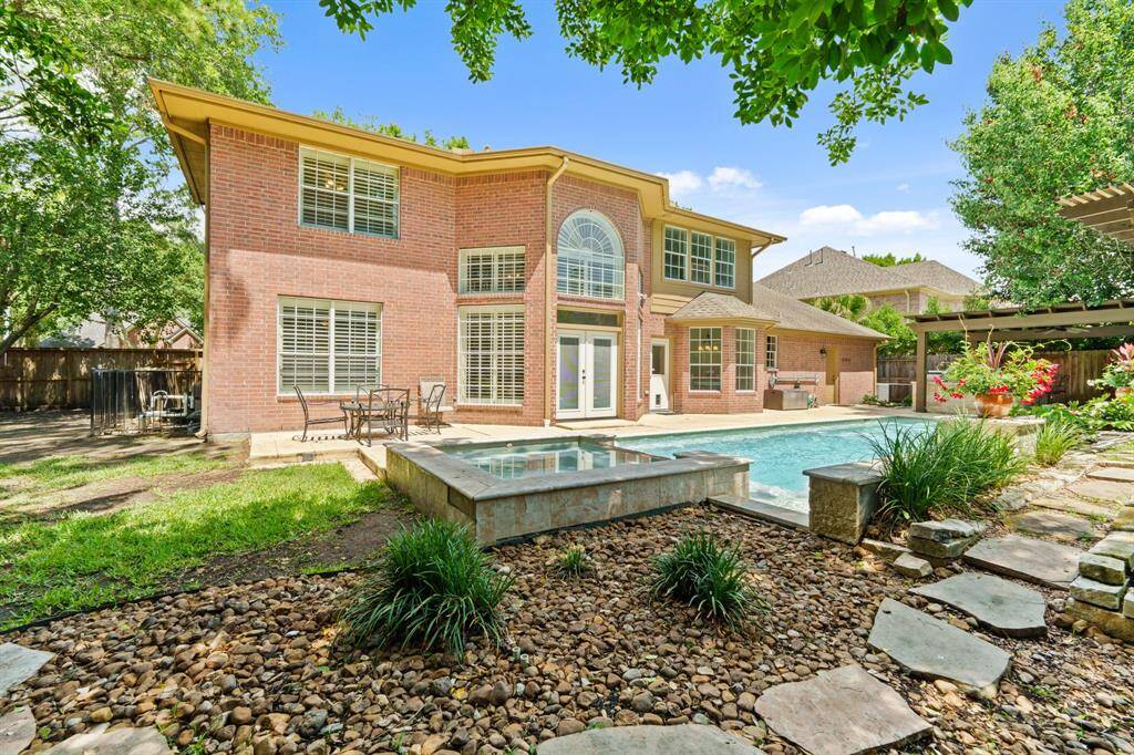 Another view of the two-story brick home with a great backyard featuring a PERGOLA, Swimming POOL and SPA. The large windows allow natural light to flood the interior, and the surrounding landscaping provides a serene and private atmosphere, perfect for relaxation and entertaining.